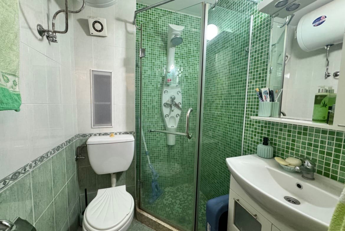 Санузел с зелеными плитками, душевой кабиной, унитазом и раковиной, подходящий для продажи недвижимости в Болгарии.