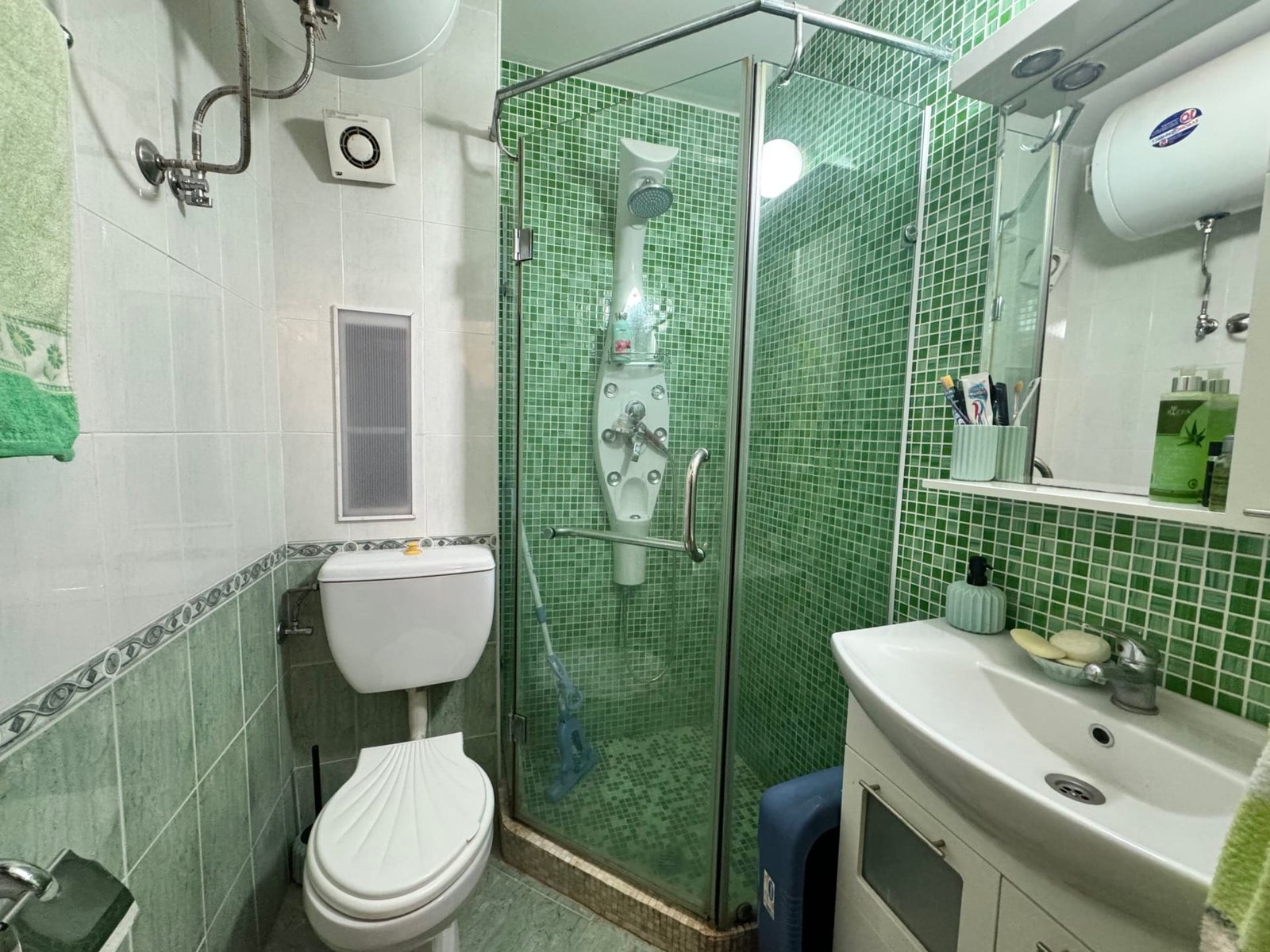 Санузел с зелеными плитками, душевой кабиной, унитазом и раковиной, подходящий для продажи недвижимости в Болгарии.