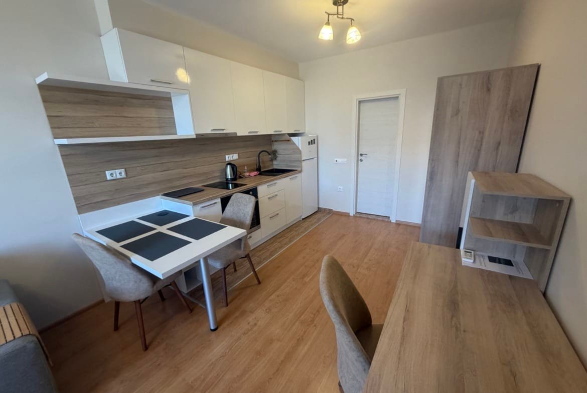 Современная кухня-студия с белыми шкафами, столом и стульями, идеальна для продажи недвижимости в Болгарии.