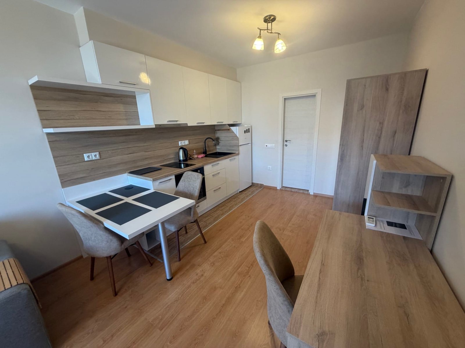 Современная кухня-студия с белыми шкафами, столом и стульями, идеальна для продажи недвижимости в Болгарии.