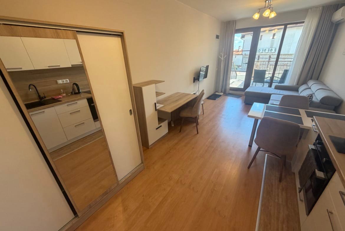 Современная квартира с меблированной гостиной, кухней и балконом, светлые тона, идеальна для покупки в Болгарии.