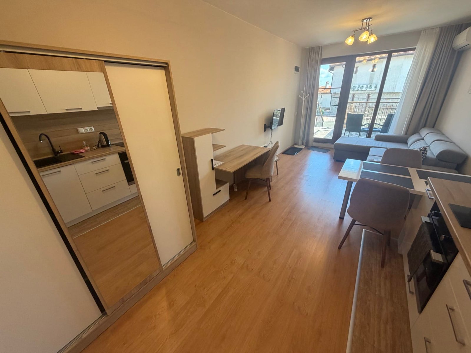 Современная квартира с меблированной гостиной, кухней и балконом, светлые тона, идеальна для покупки в Болгарии.