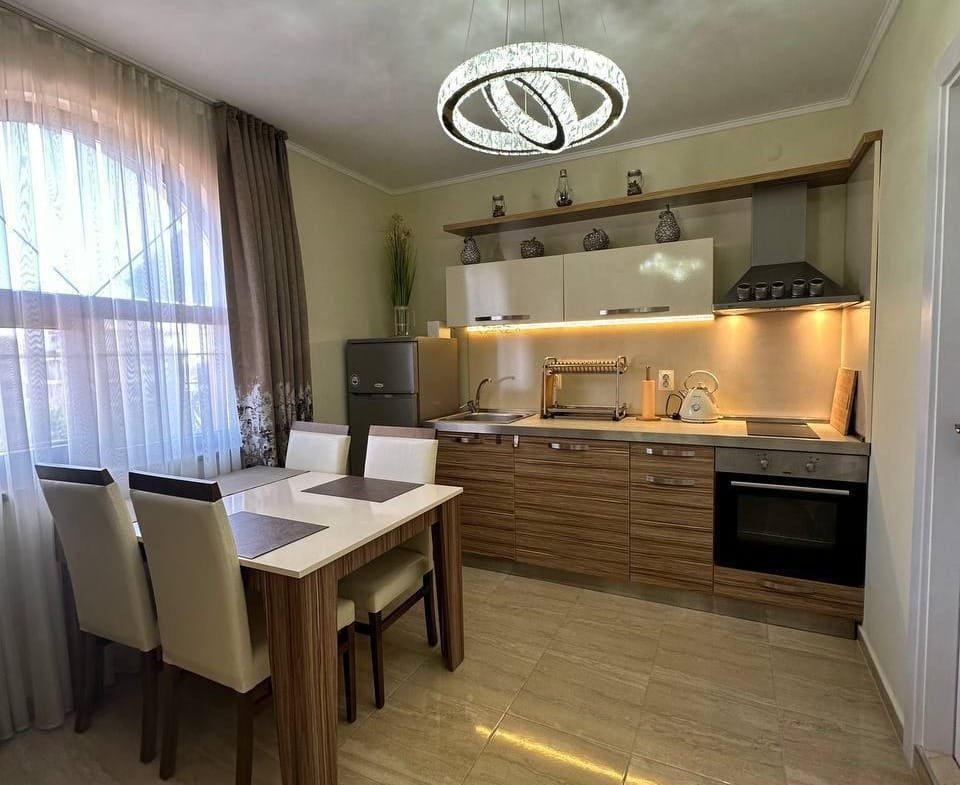 Современная кухня в светлых тонах с обеденной зоной, стильной люстрой и оборудованием для комфортного проживания в Болгарии.