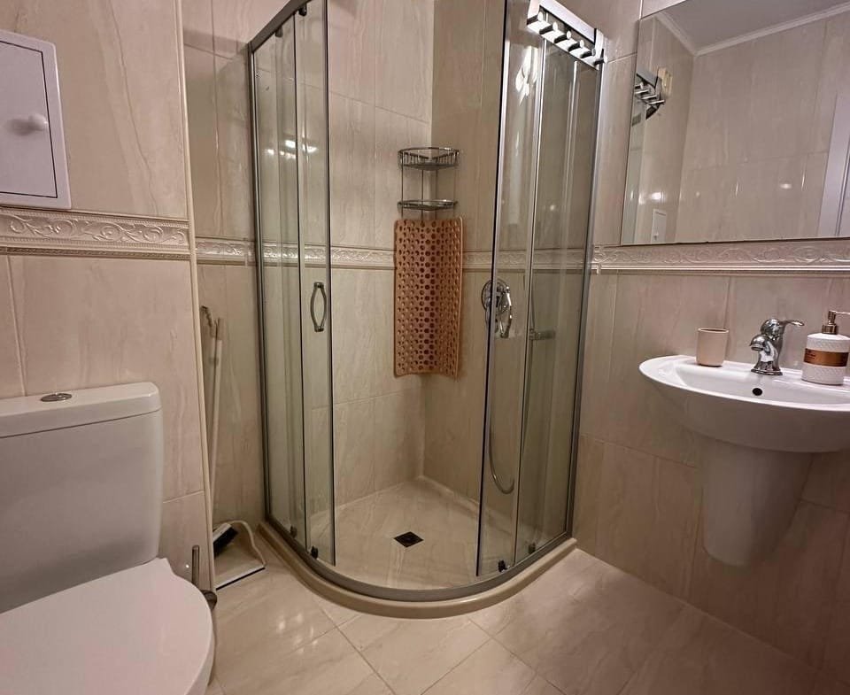 Современная ванная комната в Болгарии с душевой кабиной, унитазом и раковиной, выполненная в светлых тонах.