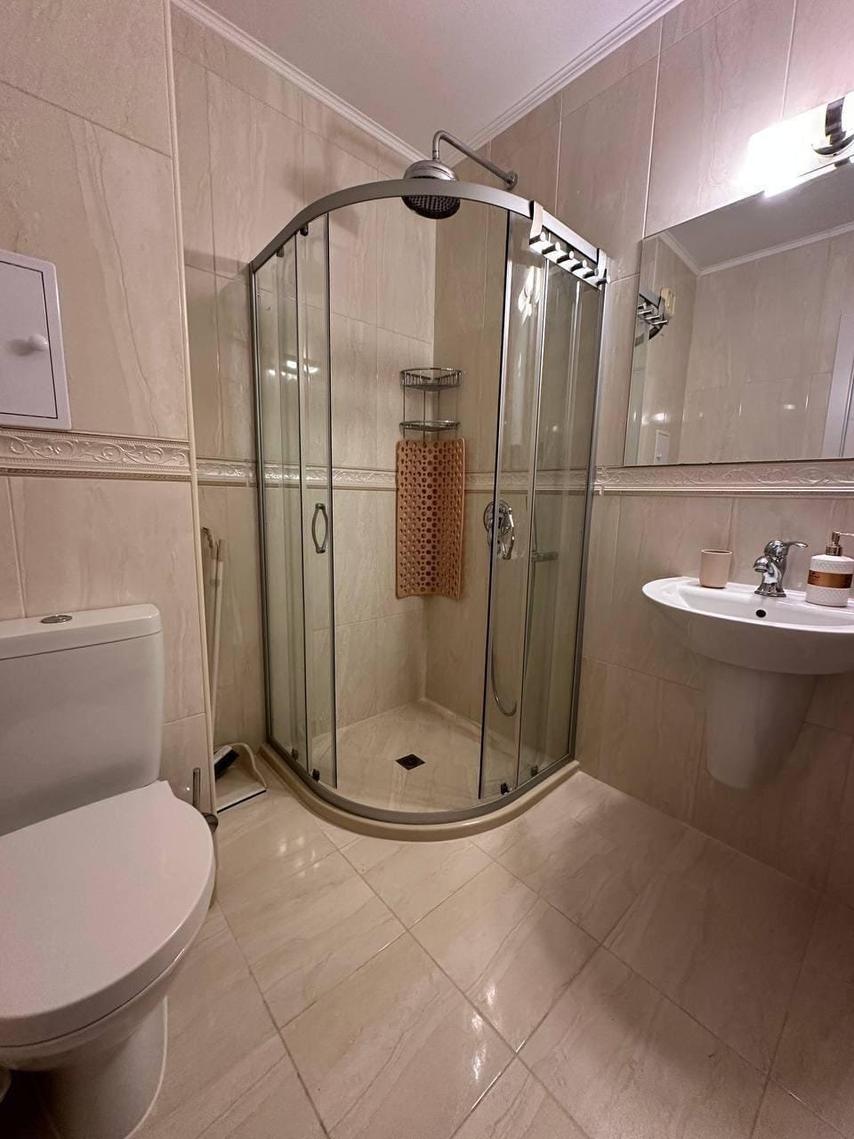 Современная ванная комната в Болгарии с душевой кабиной, унитазом и раковиной, выполненная в светлых тонах.