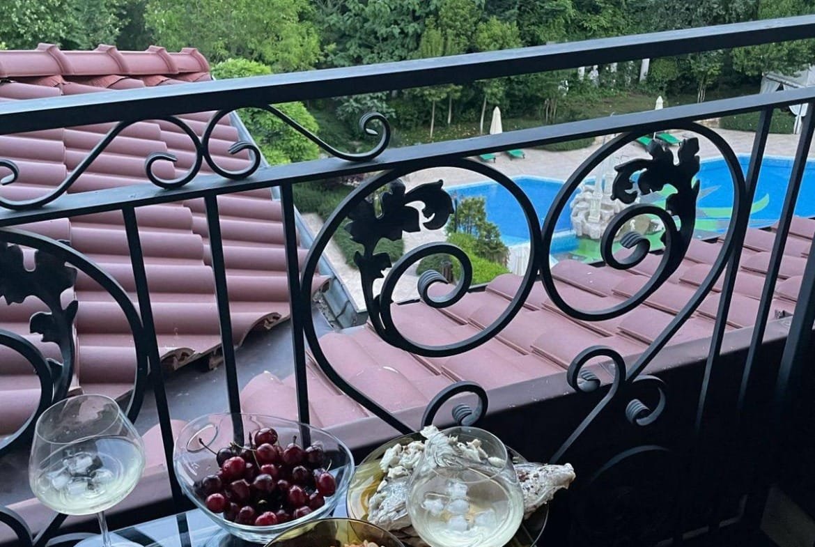 Уютный балкон с блюдами и напитками, на фоне зелени и жилого комплекса в Болгарии, идеально для продажи и покупки недвижимости.