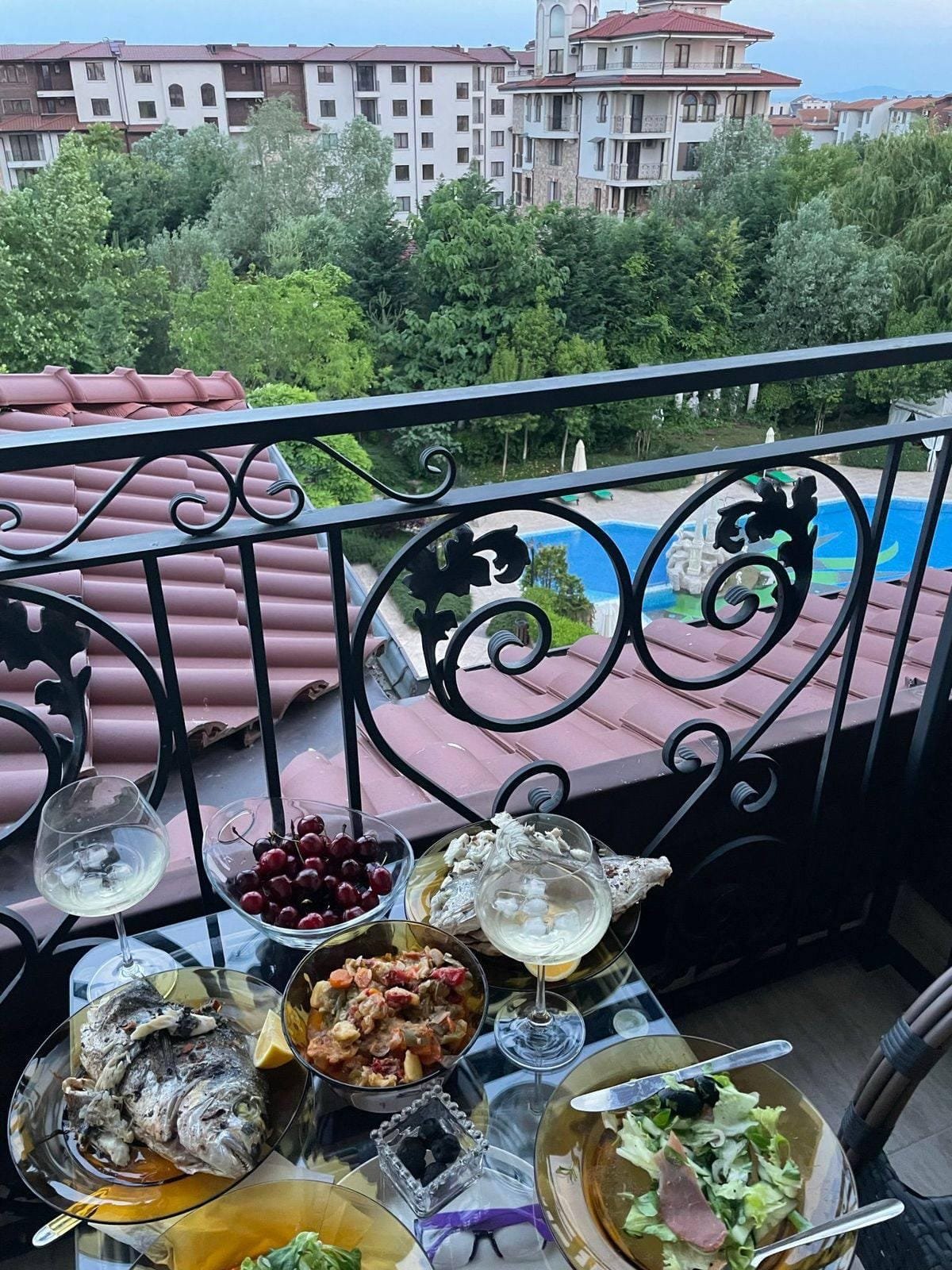 Уютный балкон с блюдами и напитками, на фоне зелени и жилого комплекса в Болгарии, идеально для продажи и покупки недвижимости.