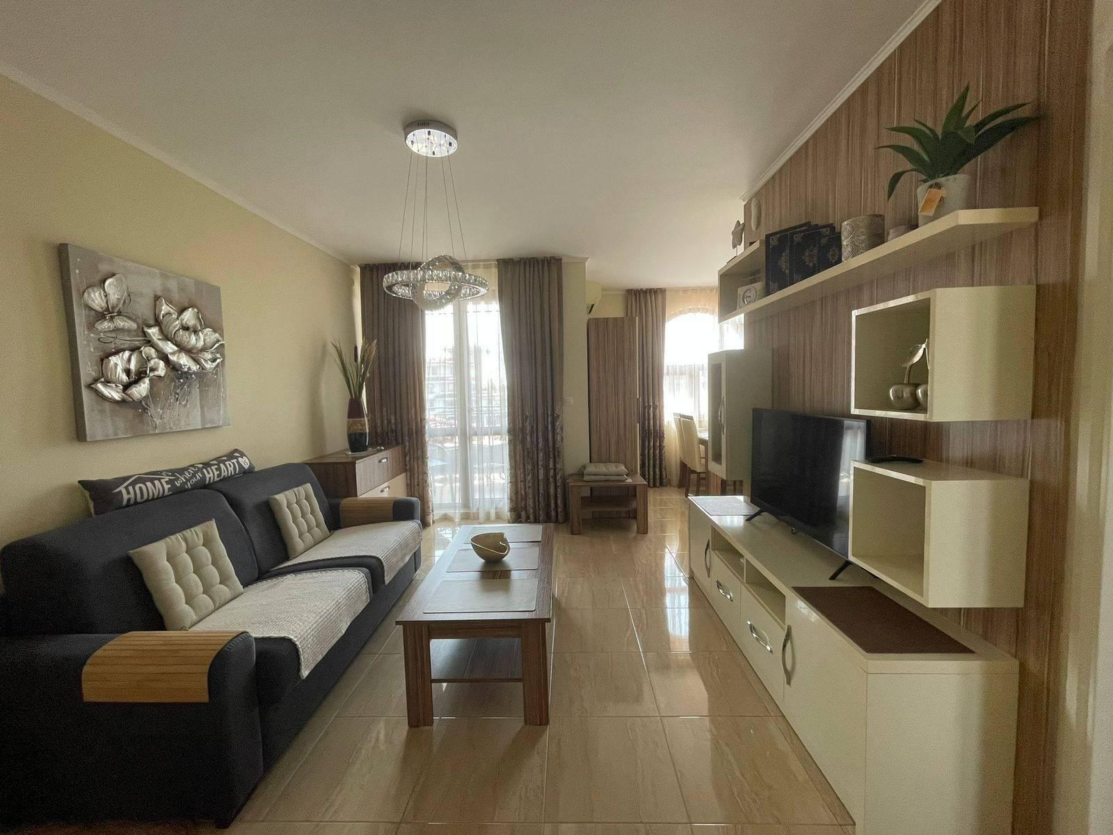 Современная уютная гостиная с телевизором, диваном и стильными элементами декора, подходящая для продажи недвижимости в Болгарии.