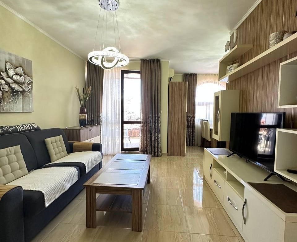 Современная гостиная с мебелью, телевизором и балконными дверями, идеально подходящая для жизни в Болгарии.