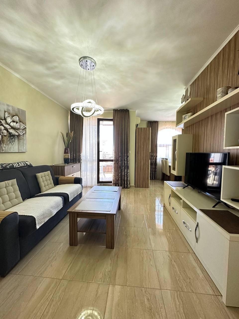 Современная гостиная с мебелью, телевизором и балконными дверями, идеально подходящая для жизни в Болгарии.