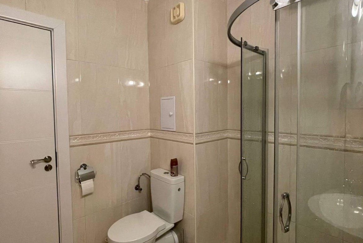 Современная ванная комната с душевой кабиной, унитазом и светлыми плитками, идеально подходит для покупки недвижимости в Болгарии.