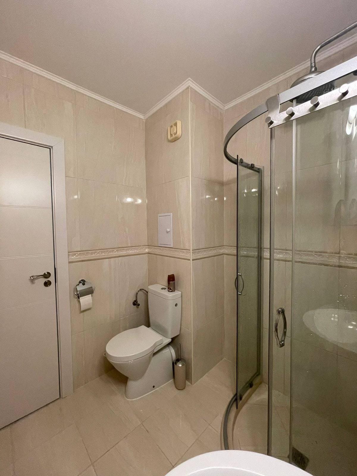 Современная ванная комната с душевой кабиной, унитазом и светлыми плитками, идеально подходит для покупки недвижимости в Болгарии.