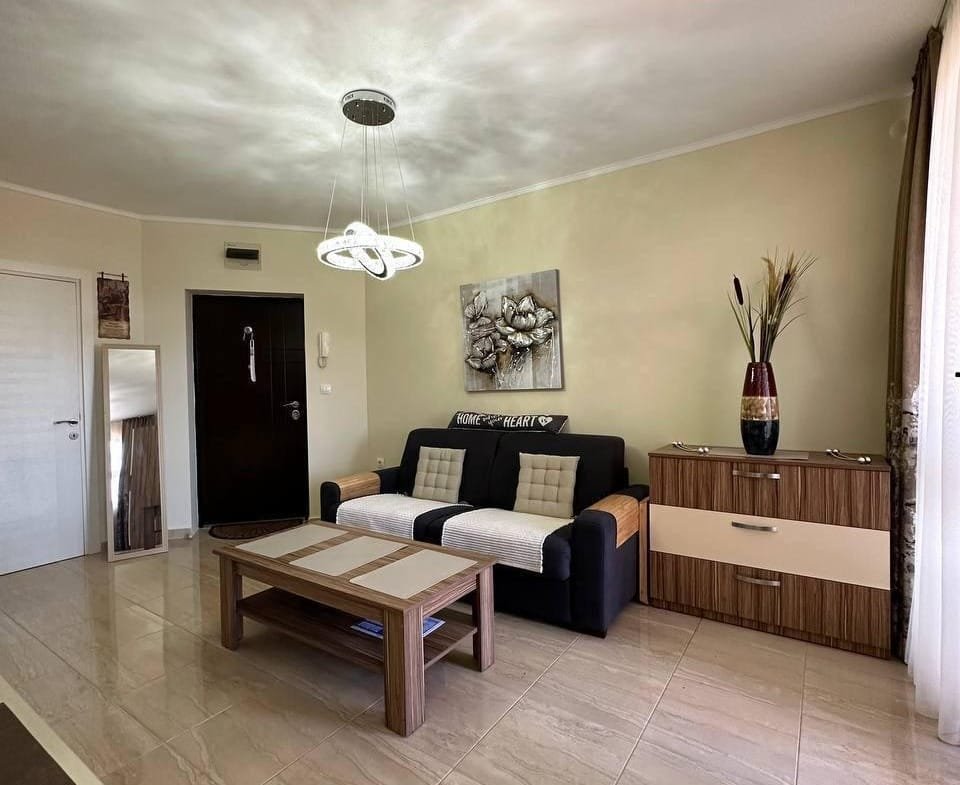 Современная гостиная с диваном, кофейным столиком и комодом, оформленная в нежных тонах для комфортного проживания в Болгарии.