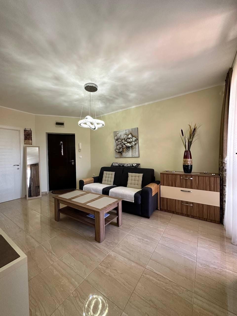 Современная гостиная с диваном, кофейным столиком и комодом, оформленная в нежных тонах для комфортного проживания в Болгарии.