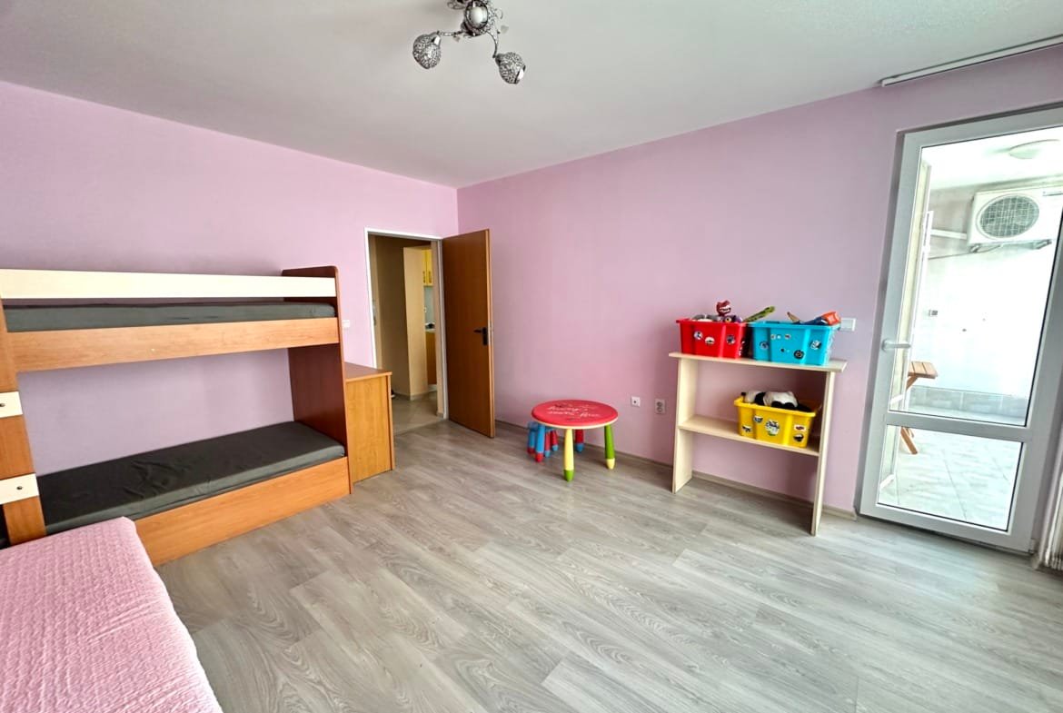 Современная комната для детей с бежевыми стенами, двухъярусной кроватью, игрушками и столом для игр в Болгарии.