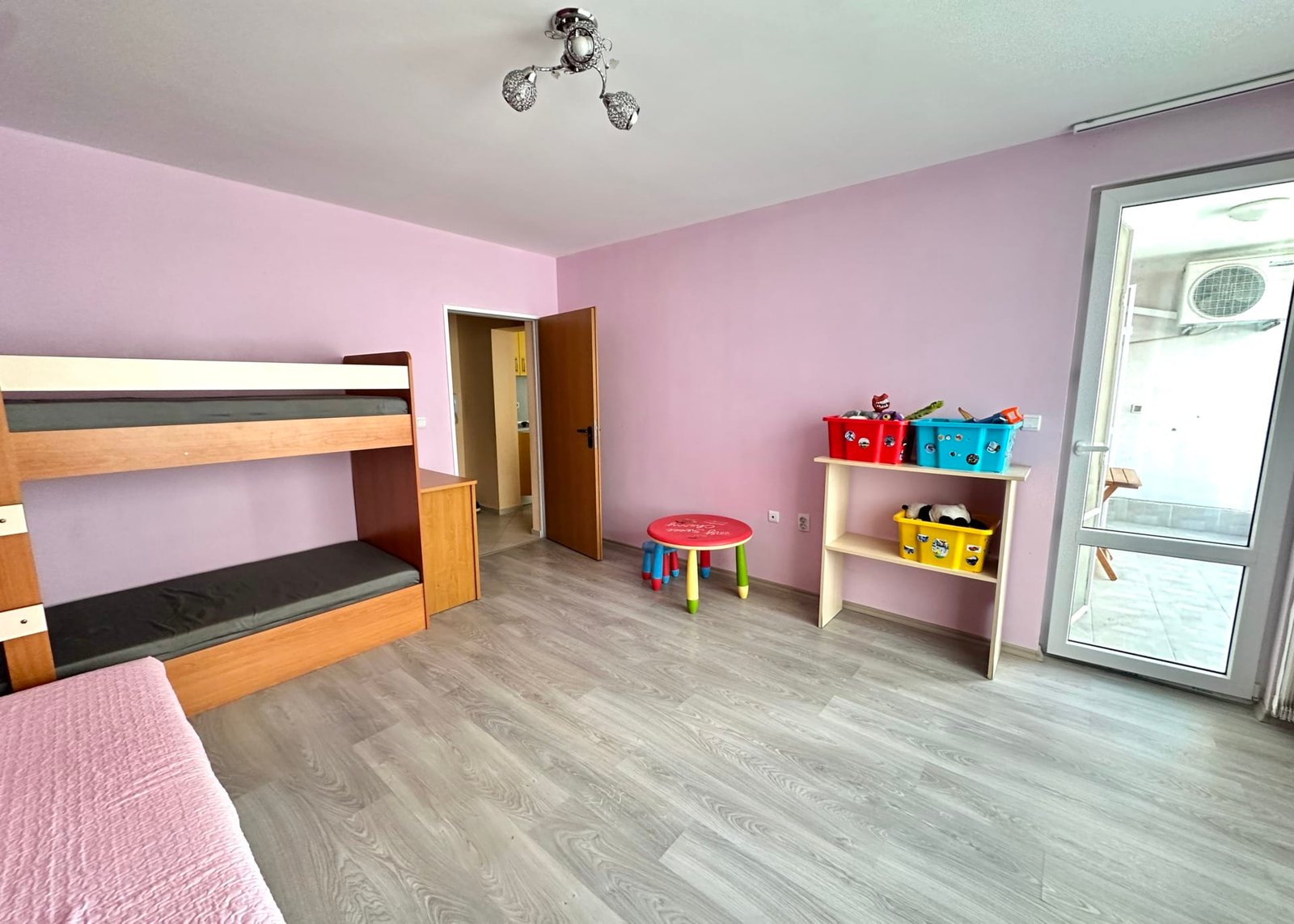 Современная комната для детей с бежевыми стенами, двухъярусной кроватью, игрушками и столом для игр в Болгарии.