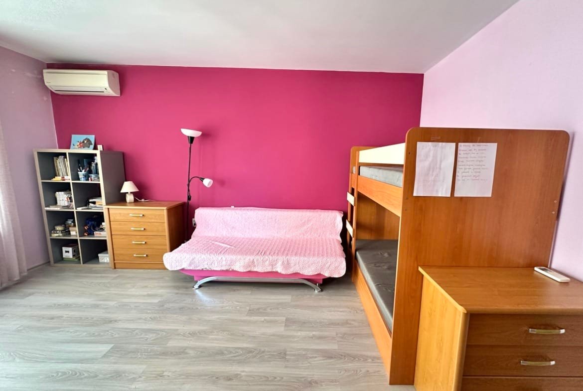 Светлая комната с розовой стеной, двухъярусной кроватью и мебелью для хранения, подходит для аренды в Болгарии.