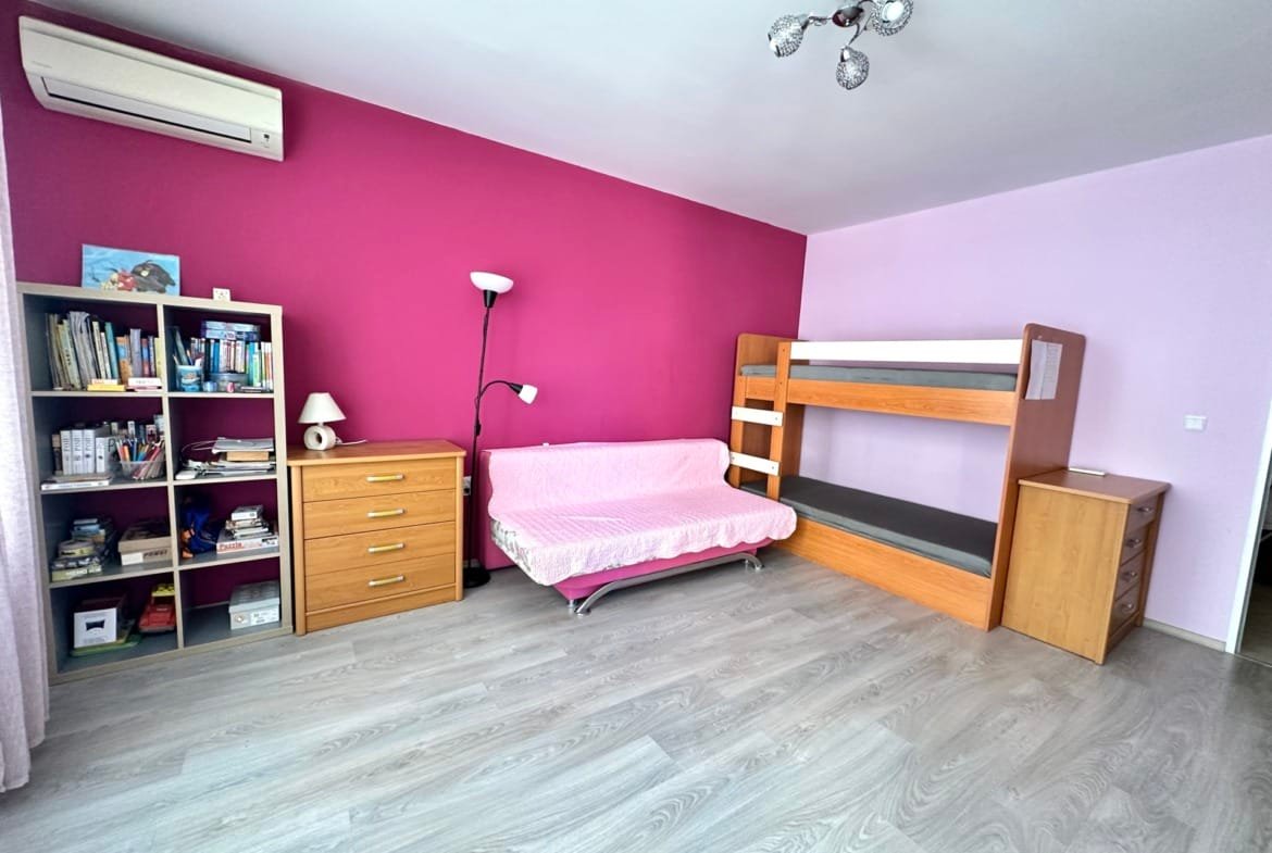 Яркая комната с розовыми стенами, двухъярусной кроватью, уютным диваном и книжным шкафом, подходящая для покупки недвижимости в Болгарии.