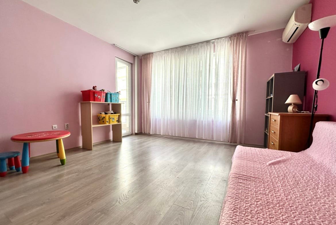 Светлая комната с розовыми стенами, детской мебелью и большими окнами, идеальная для покупки недвижимости в Болгарии.