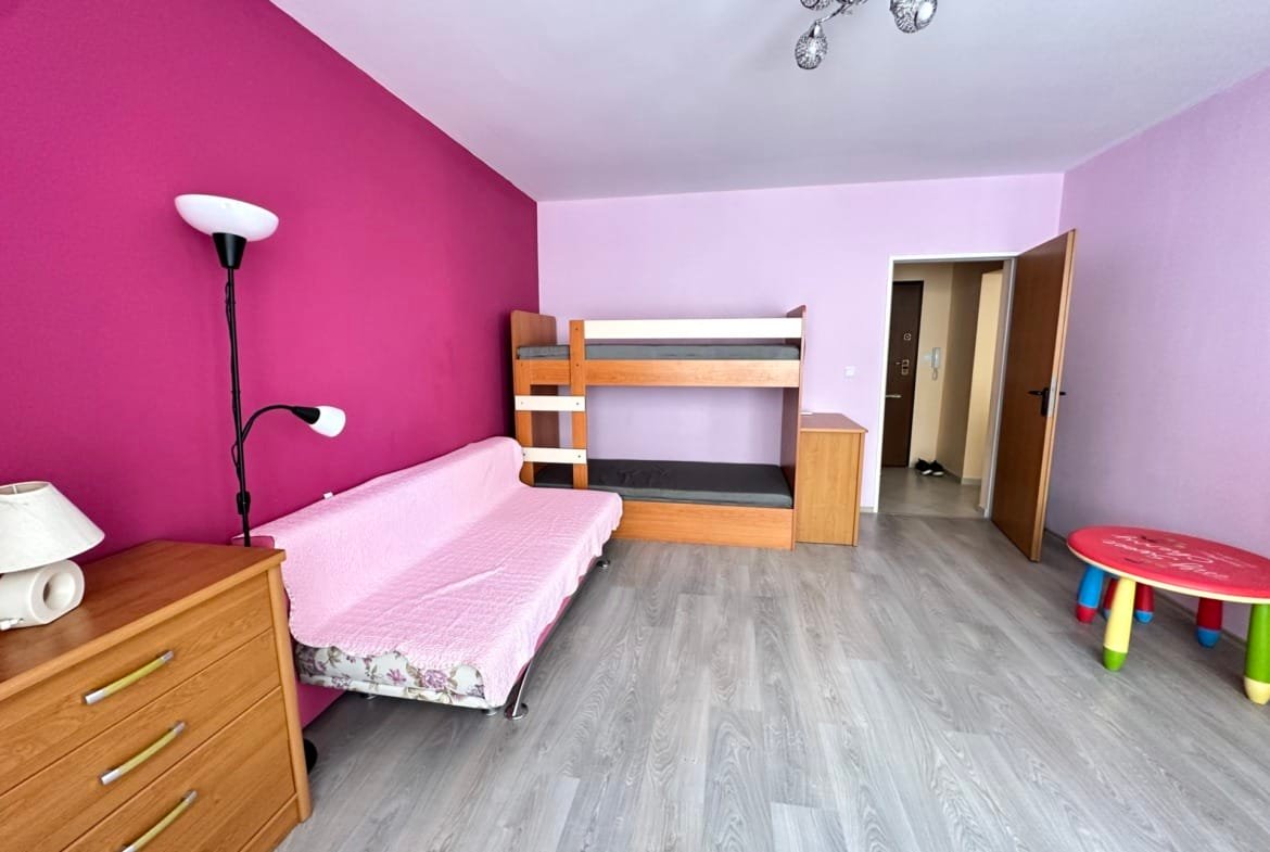 Уютная комната с розовыми стенами, двухъярусной кроватью, диваном и детским столом, идеальная для жилья в Болгарии.