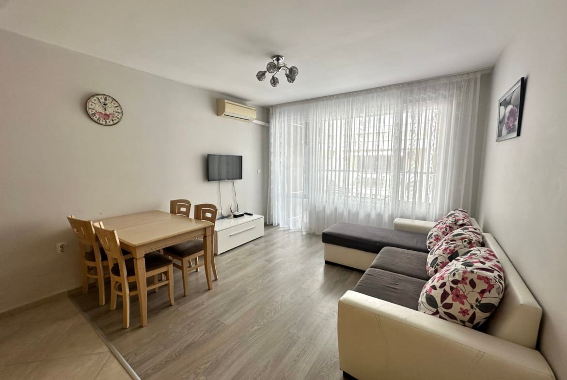 Современная квартира в Болгарии с уютной меблировкой, обеденным столом и светлыми шторами, идеально подходит для покупки или аренды.