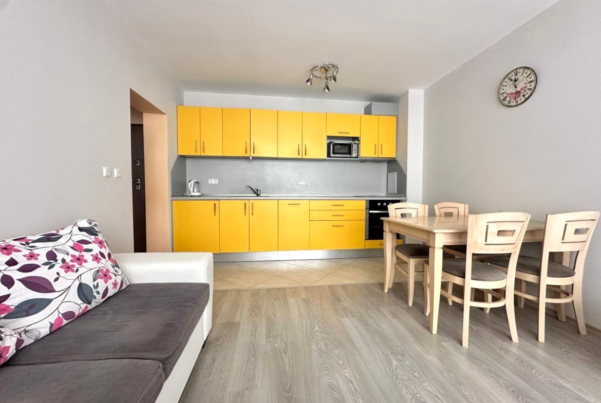 Кухня-гостиная с желтыми шкафами, столом и стульями, диваном и часами, подходит для продажи недвижимости в Болгарии.