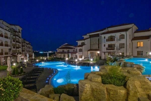 Ночной вид на курортный комплекс с бассейном и современными зданиями, подчеркивающий привлекательность недвижимости в Болгарии.