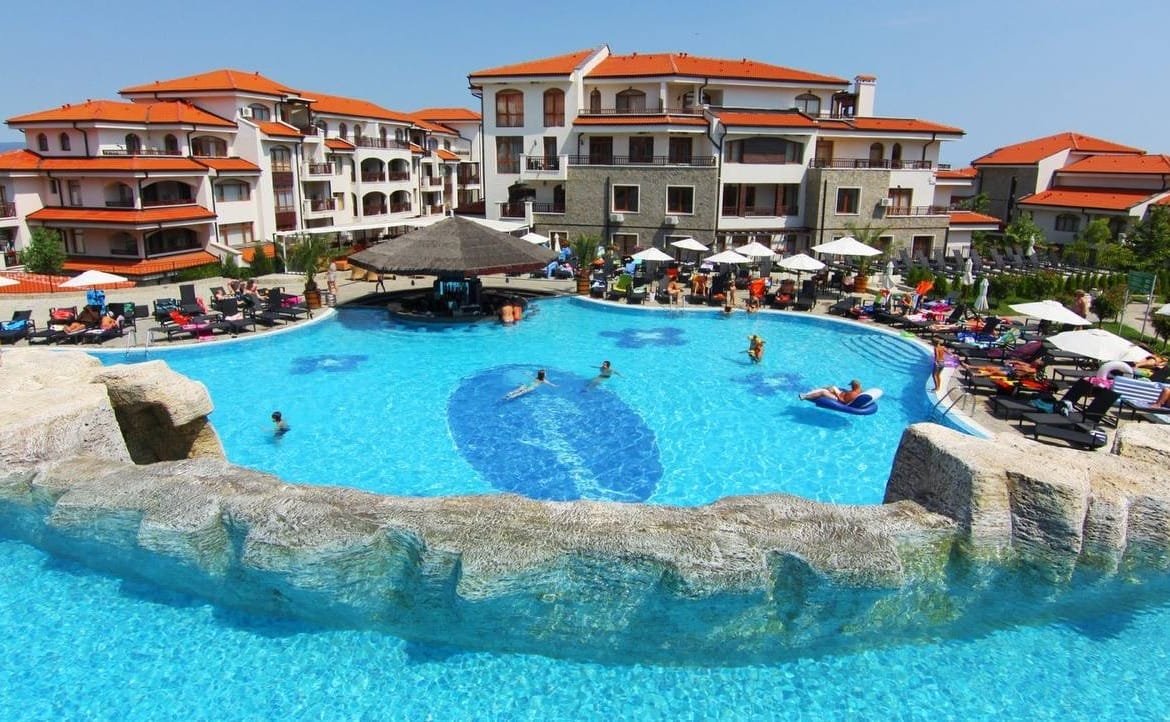 Современный жилой комплекс у моря с бассейном в Болгарии, зонтиками, шезлонгами и отдыхающими. Идеальное место для покупки недвижимости.