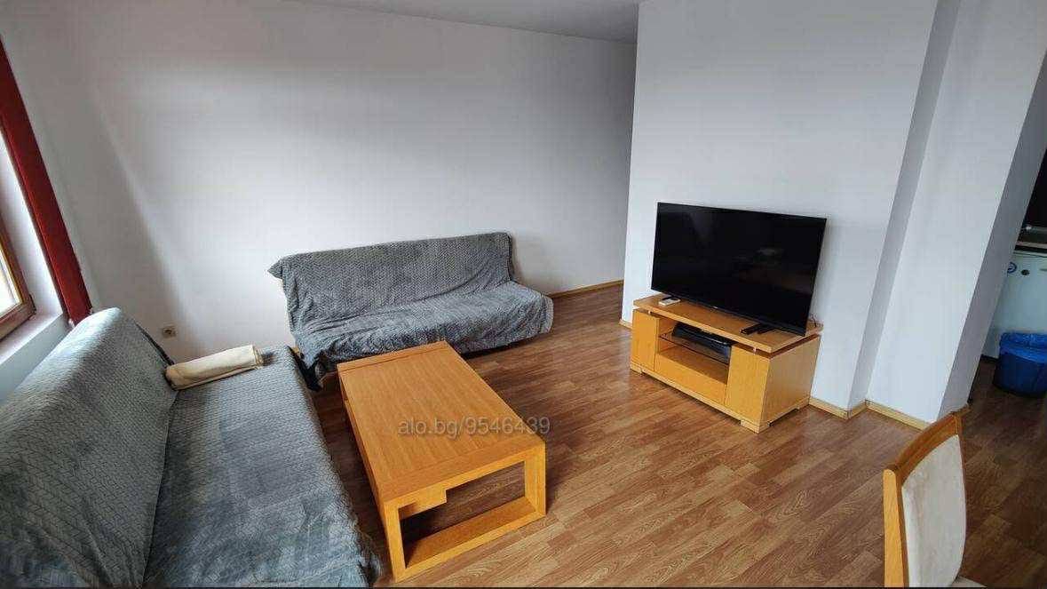 Современная гостиная в Болгарии с деревянной мебелью, телевизором и светлыми стенами, готовая к продаже или аренде.