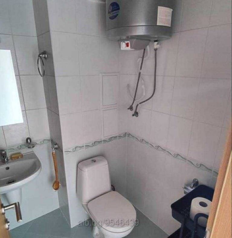 Небольшой санузел с унитазом, раковиной и бойлером, отделка светлыми плитками, подходит для покупки недвижимости в Болгарии.