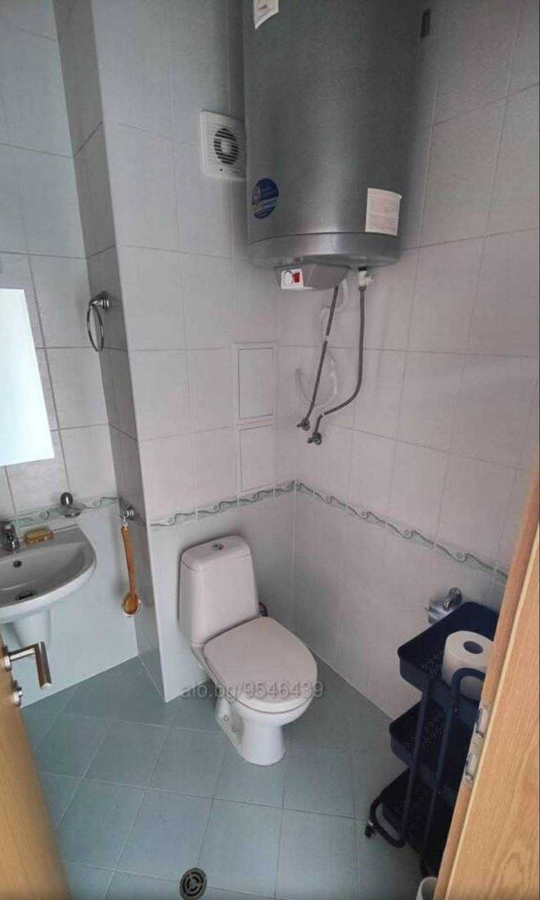 Небольшой санузел с унитазом, раковиной и бойлером, отделка светлыми плитками, подходит для покупки недвижимости в Болгарии.