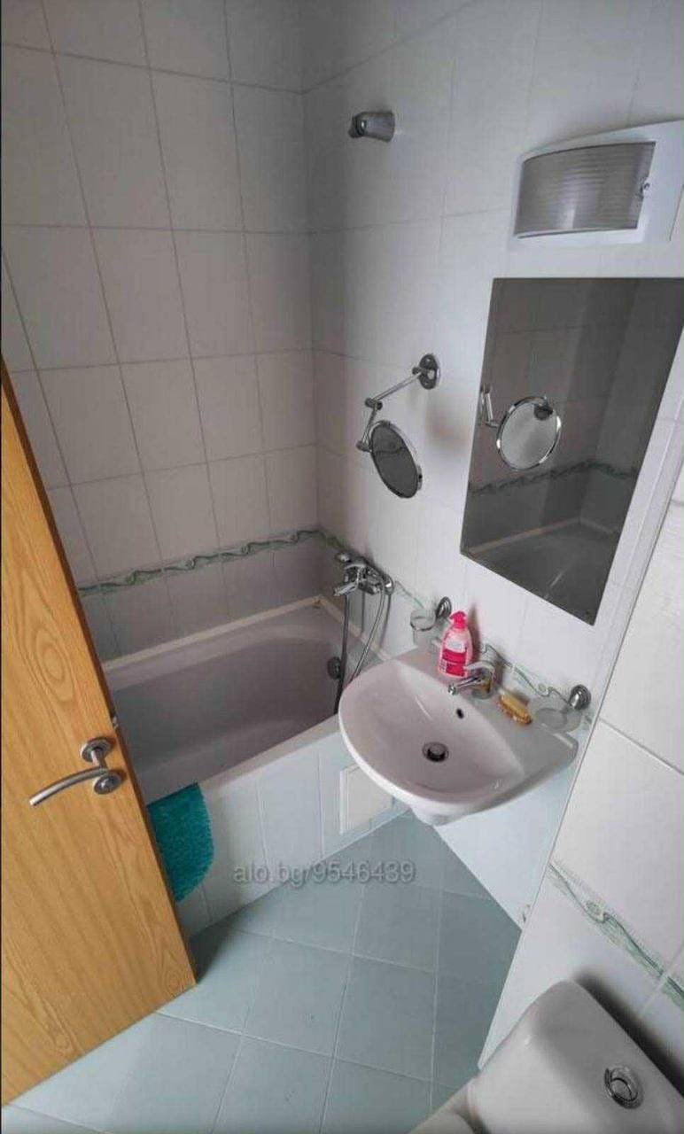 Современная ванная комната с ванной, раковиной и зеркалом в болгарской квартире, готовой к продаже.