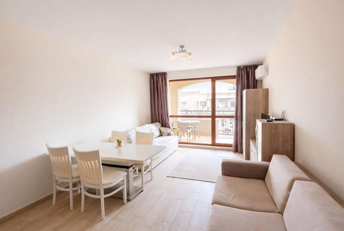 Современная квартира в Болгарии с уютной мебелью, обеденным столом и балконом, предлагающая комфорт для жизни и отдыха.