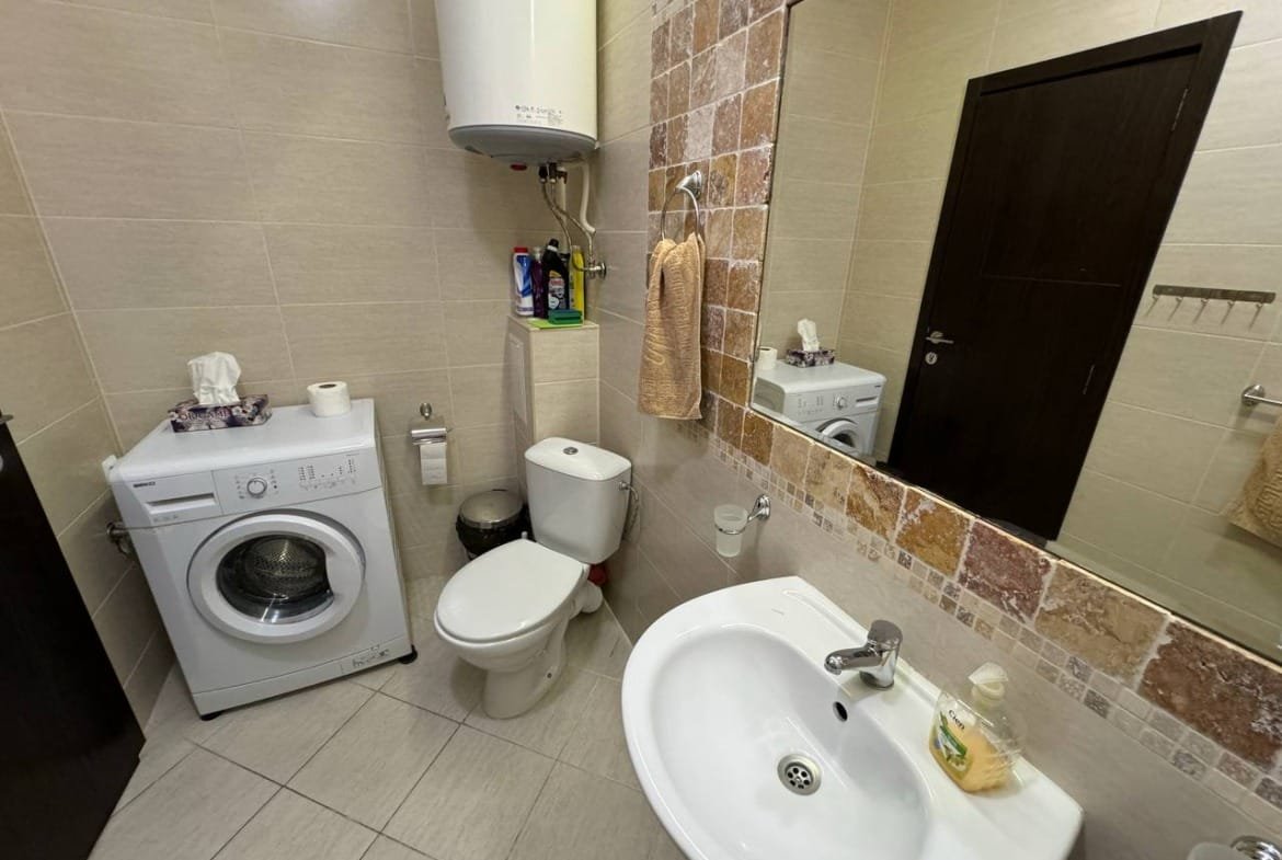 Санузел с стиральной машиной, унитазом и раковиной, оформленный в светлых тонах, подходит для жилья в Болгарии.