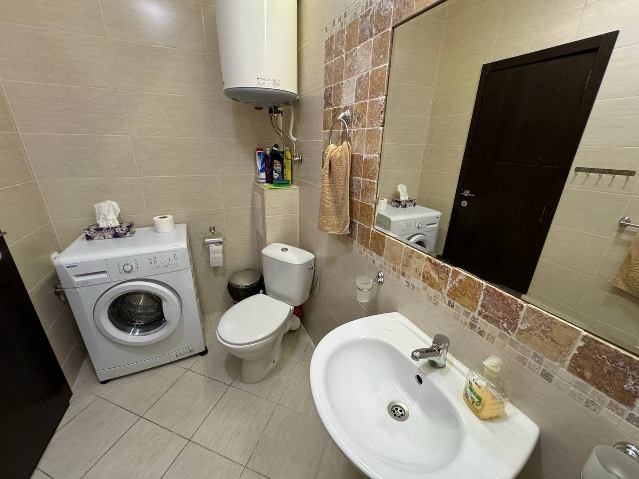 Санузел с стиральной машиной, унитазом и раковиной, оформленный в светлых тонах, подходит для жилья в Болгарии.