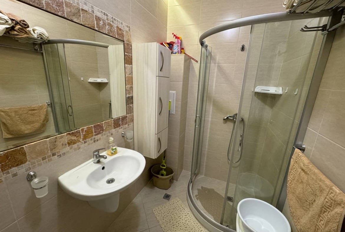 Уютная ванная комната с душевой кабиной, раковиной и зеркалом, отделанная плиткой, идеальная для продажи недвижимости в Болгарии.