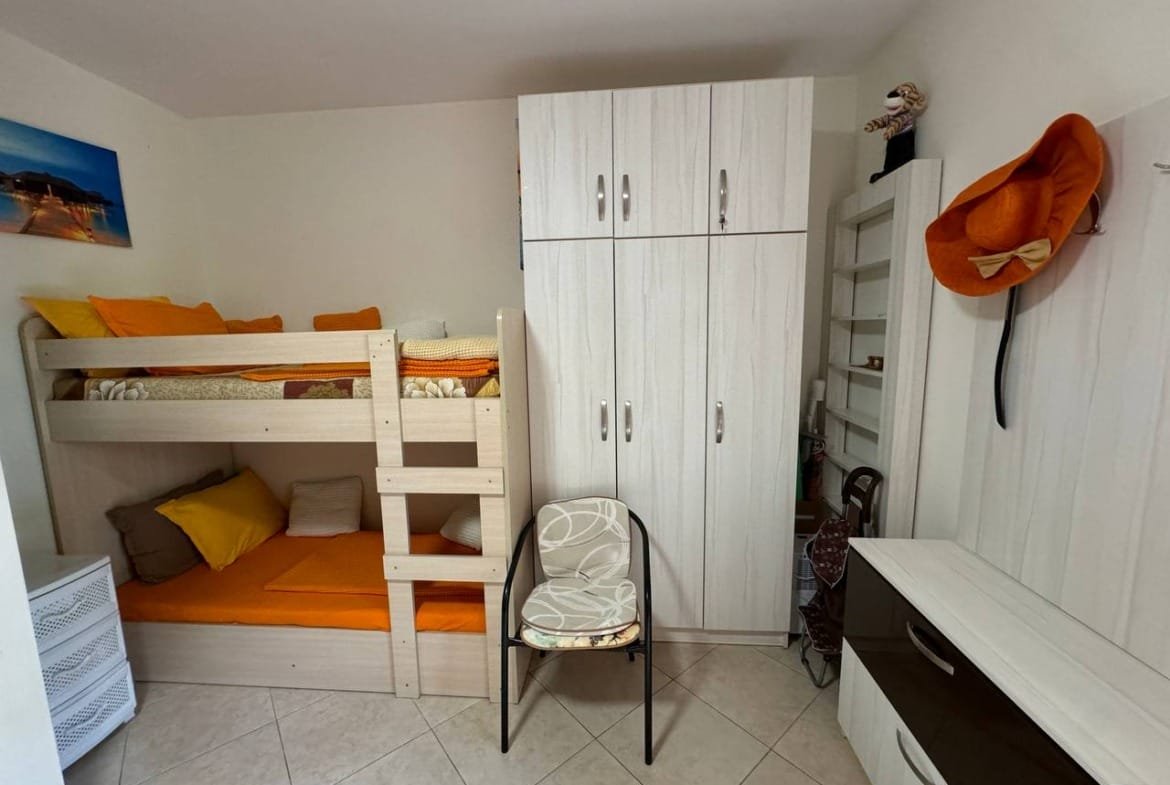 Комната с двухъярусной кроватью, светлыми стенами и яркими подушками, подходит для аренды или покупки недвижимости в Болгарии.