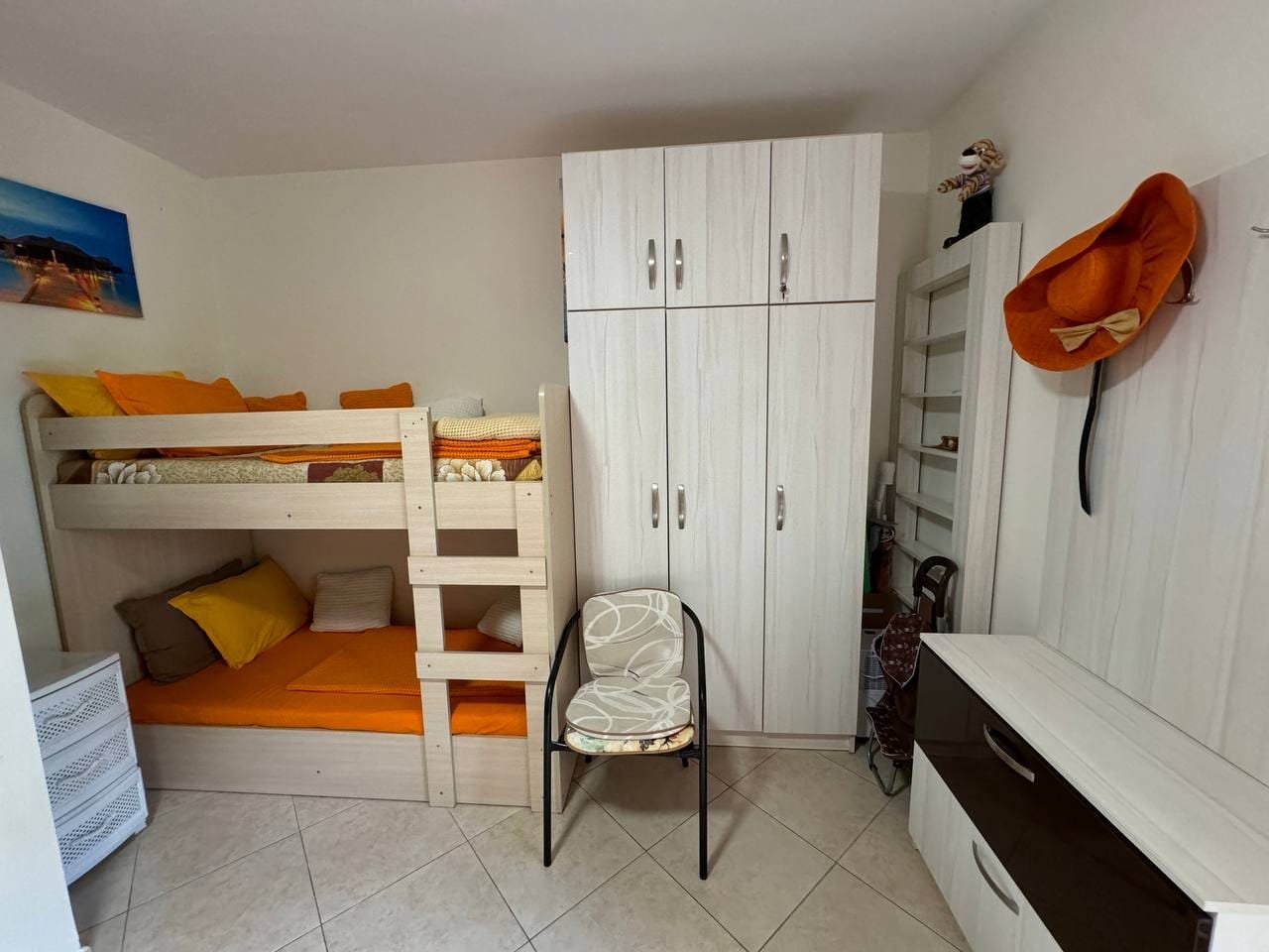 Комната с двухъярусной кроватью, светлыми стенами и яркими подушками, подходит для аренды или покупки недвижимости в Болгарии.