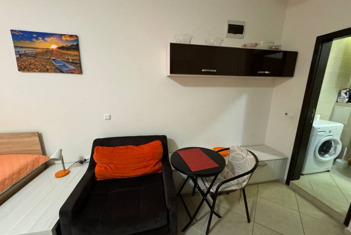 Современная квартира в Болгарии с уютной мебелью, столиком и стиральной машиной, подходит для комфортного проживания и отдыха.