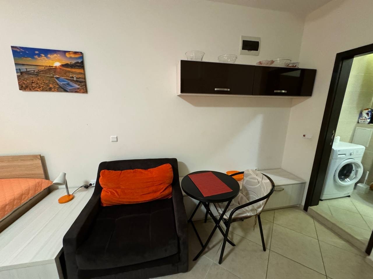 Современная квартира в Болгарии с уютной мебелью, столиком и стиральной машиной, подходит для комфортного проживания и отдыха.