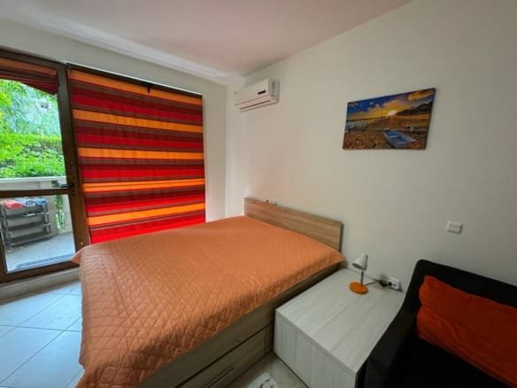 Уютная спальня с оранжевым покрывалом, балконом и яркими шторами, идеальная для отдыха в Болгарии.