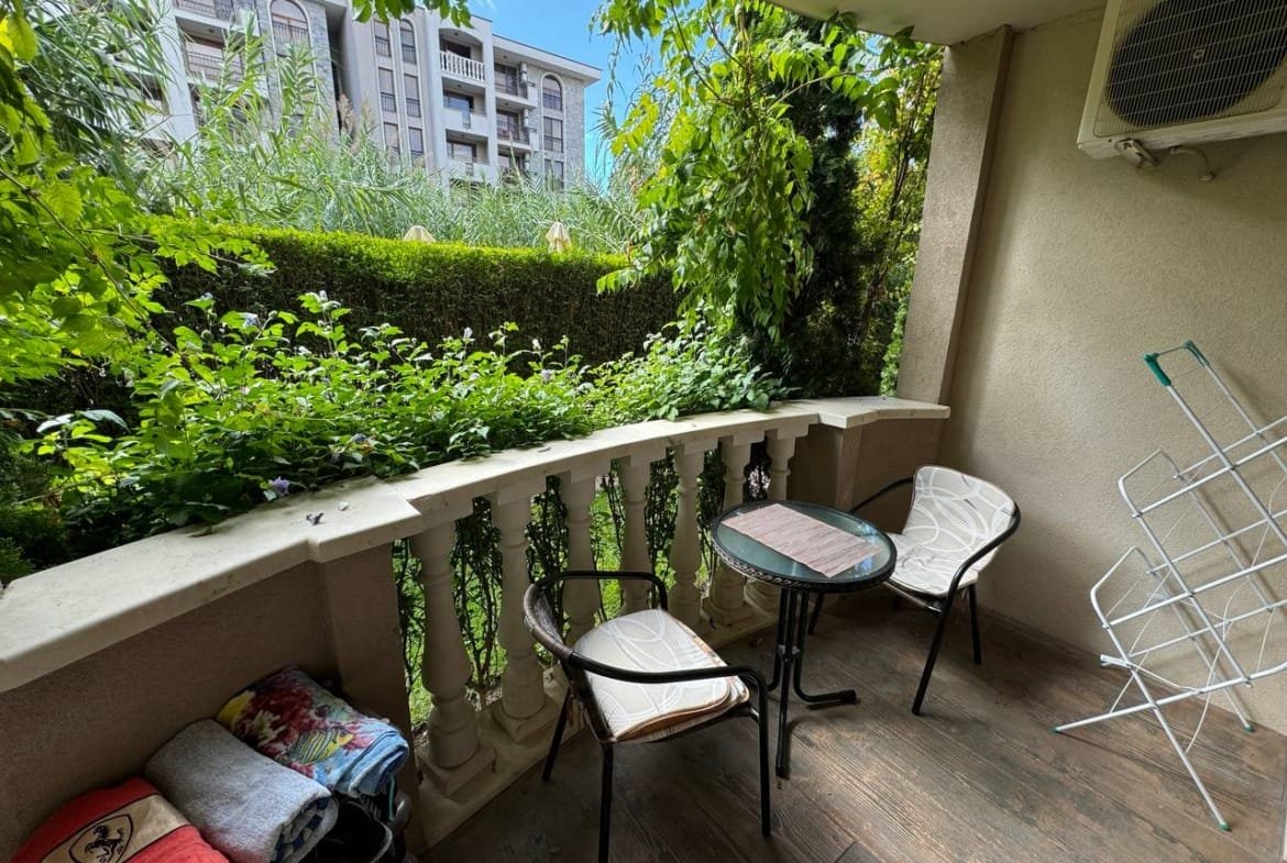 Уютный балкон с двумя стульями и столом, окруженный зеленью, идеальное место для отдыха в Болгарии.