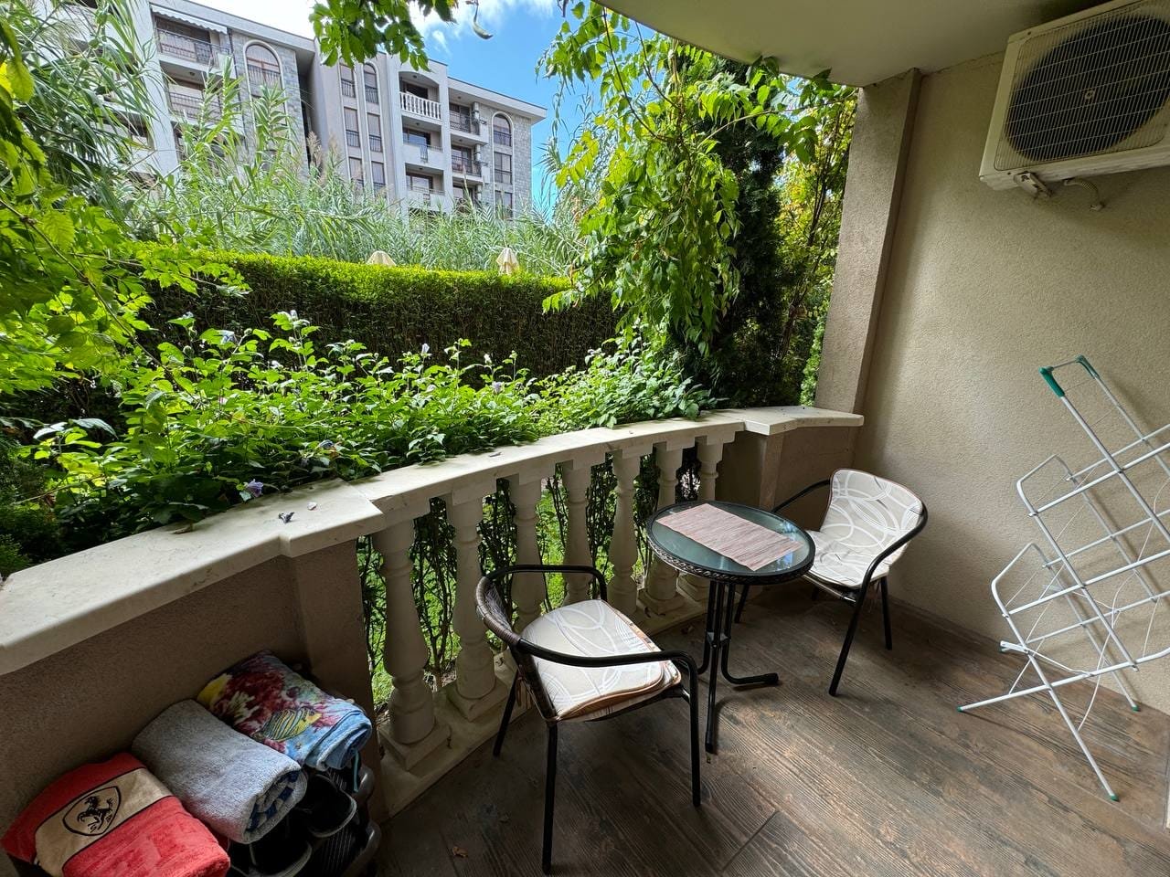 Уютный балкон с двумя стульями и столом, окруженный зеленью, идеальное место для отдыха в Болгарии.