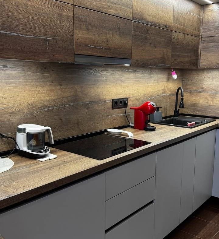 Современная кухня с деревянными фасадами, черной столешницей, варочной панелью и кофемашиной, идеальна для жизни в Болгарии.