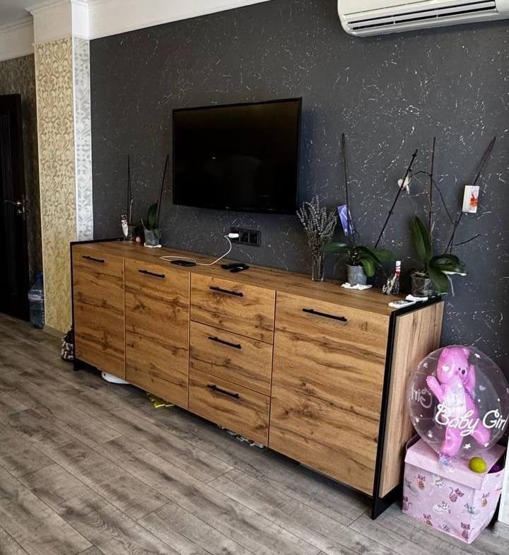 Современный интерьер квартиры в Болгарии с деревянным комодом, телевизором и элементами декора в нейтральных тонах.