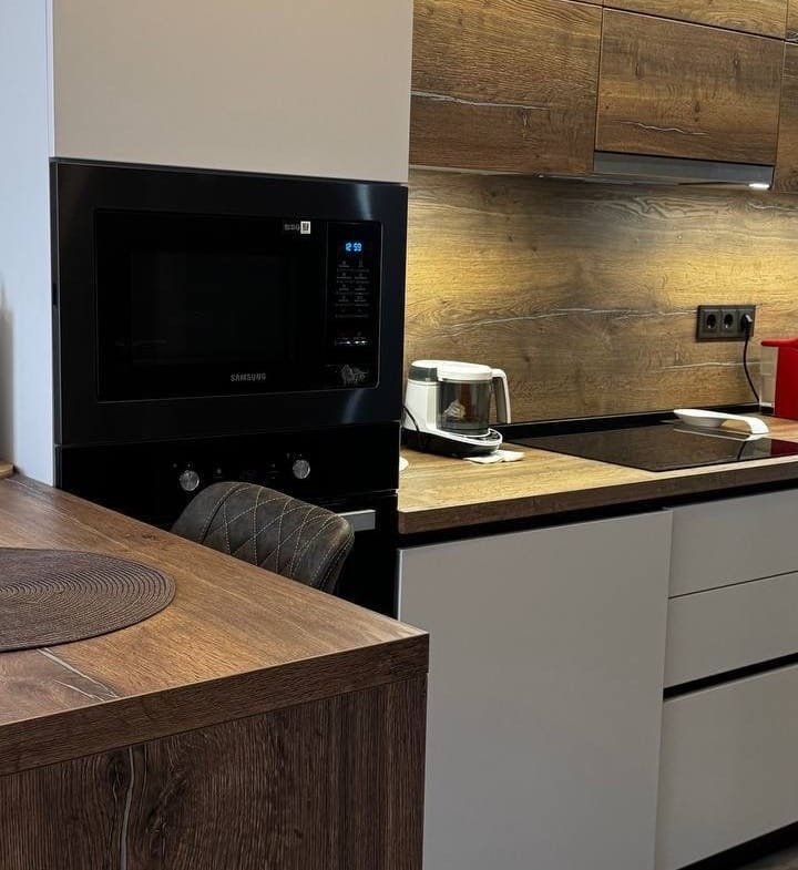 Современная кухонная мебель с деревянными фасадами, встроенной техникой и стильным освещением, идеальна для продажи недвижимости в Болгарии.