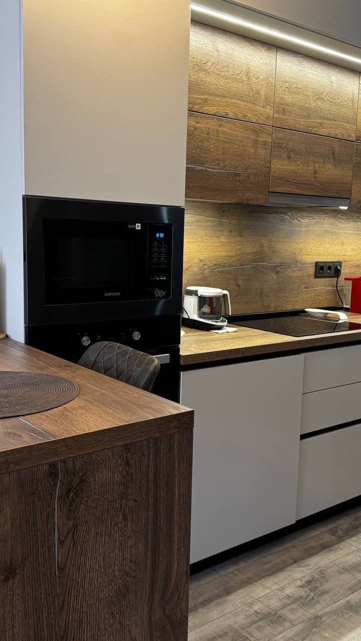 Современная кухонная мебель с деревянными фасадами, встроенной техникой и стильным освещением, идеальна для продажи недвижимости в Болгарии.