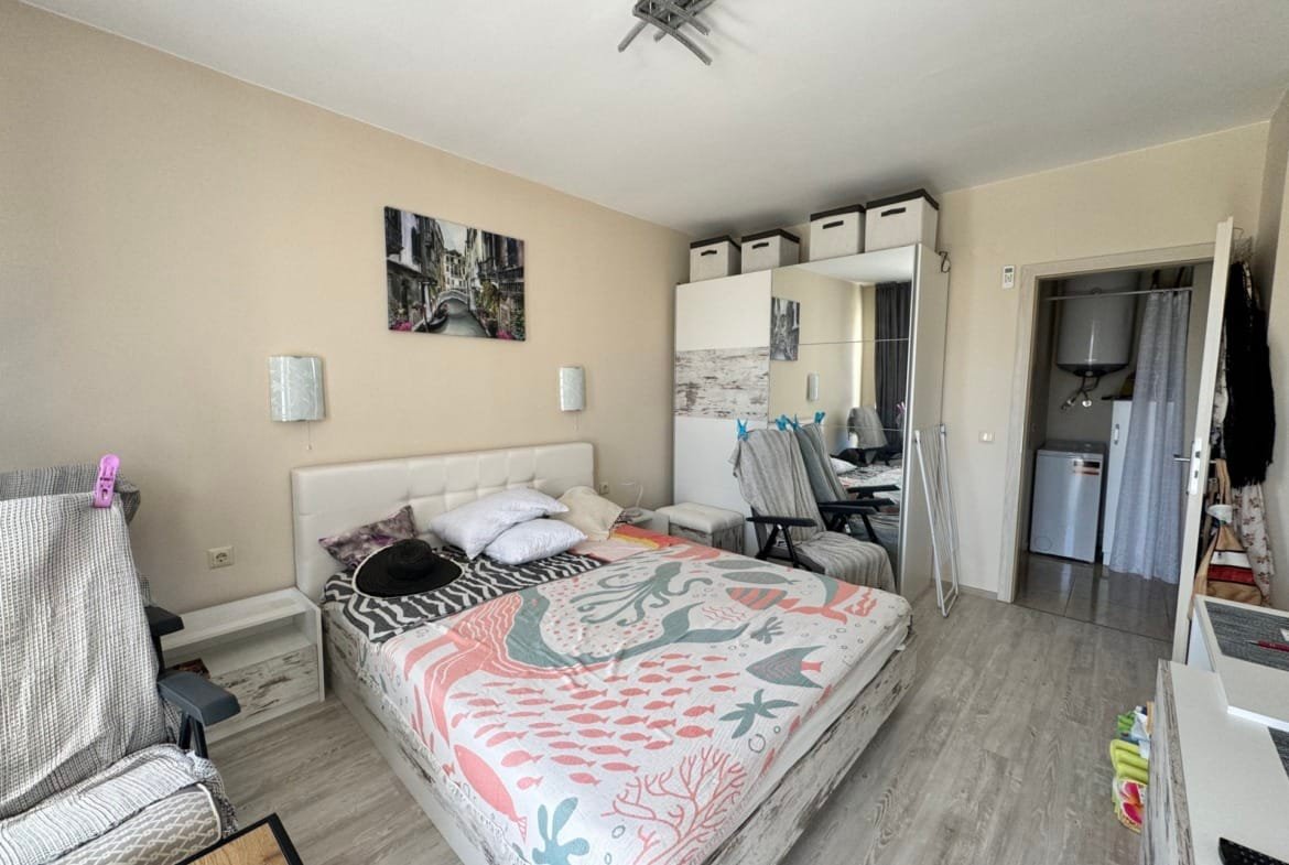 Уютная спальня с двуспальной кроватью, светлыми стенами и современным интерьером, идеальна для покупки недвижимости в Болгарии.