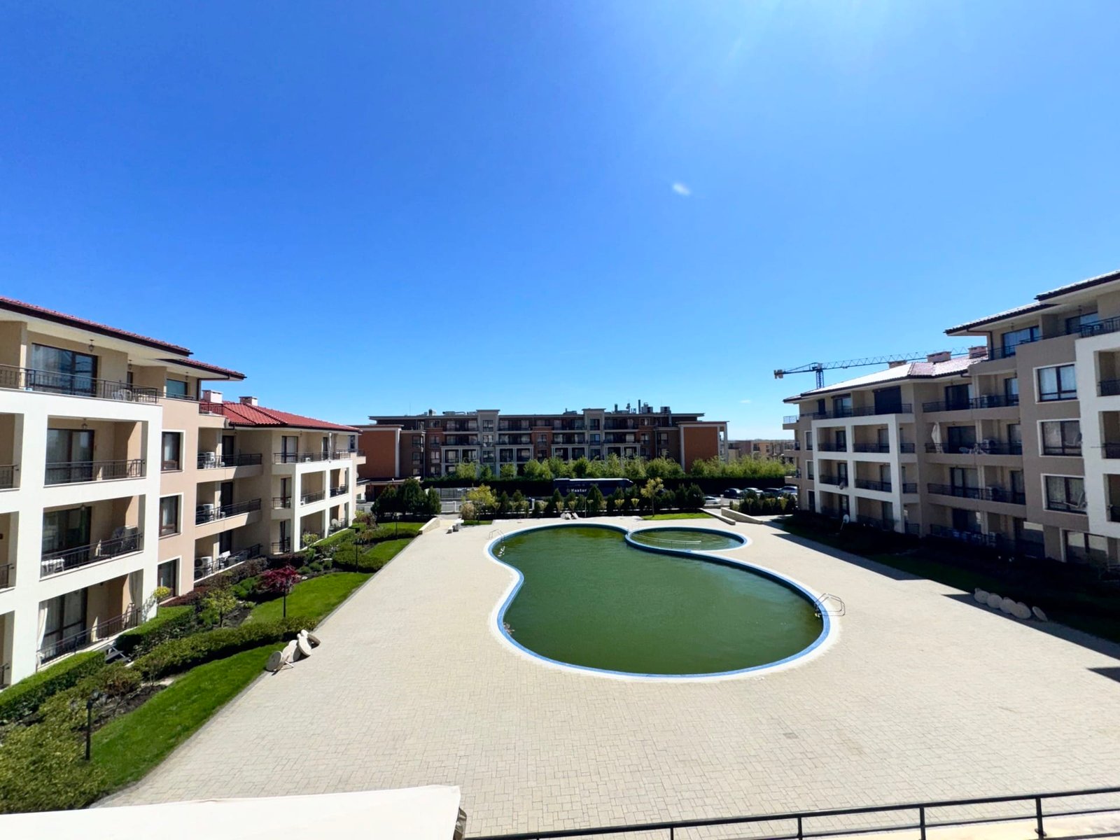 Современный жилой комплекс с бассейном и зелеными насаждениями Современный комплекс с бассейном, зелеными насаждениями и светлой архитектурой, предлагающий жилье в Болгарии.