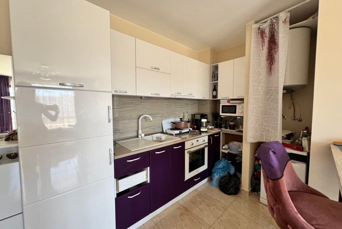 Современная кухня с белыми и фиолетовыми фасадами, компактная планировка, бытовая техника и обеденные стулья.